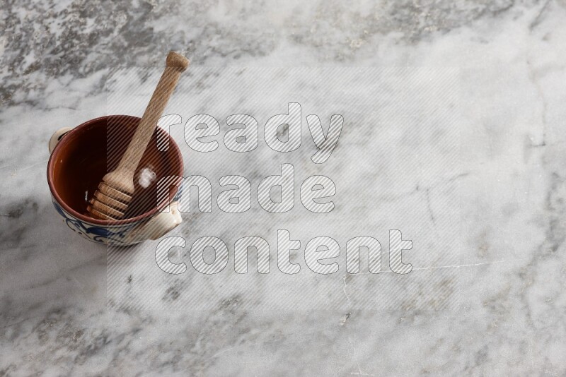 Decorative pottery pot with wooden honey dipper in it on grey marble background