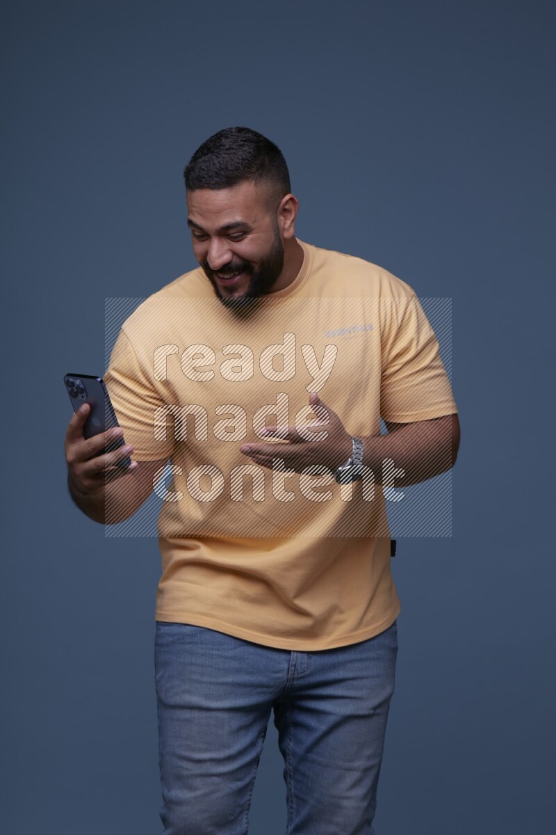 رجل يرتدي قميص اصفر باكمام قصيرة وبنطال جينز ازرق يقوم بمحادثة مرئية باستخدام جواله