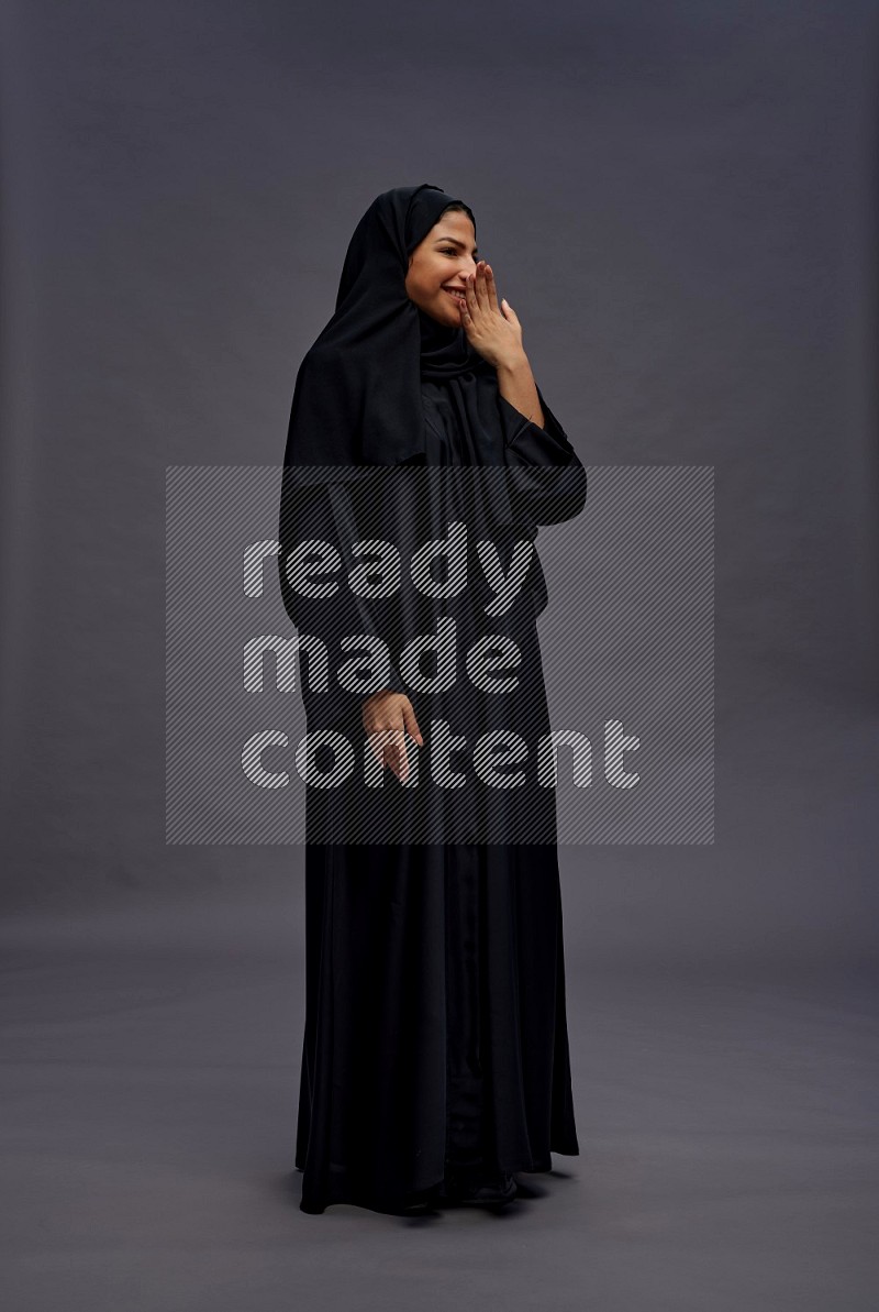 Saudi woman wearing Abaya standing interacting with the camera on gray background