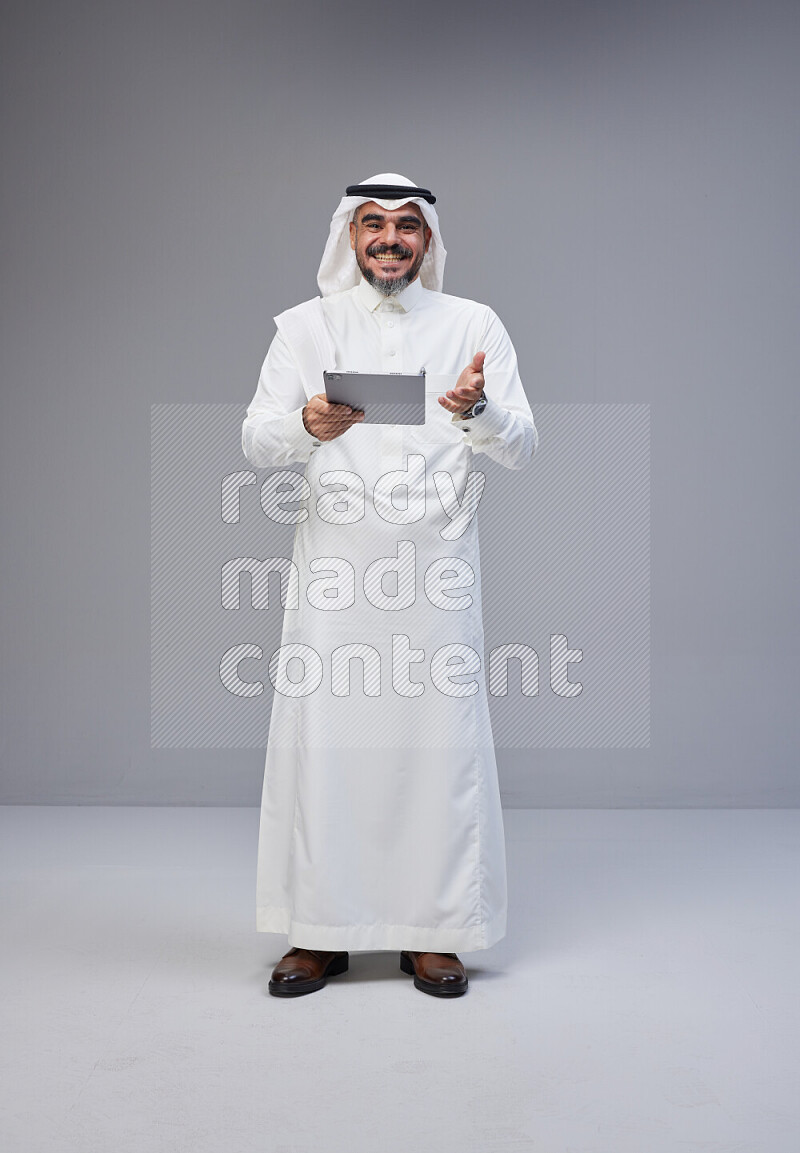 Saudi man Wearing Thob and white Shomag standing working on tablet on Gray background