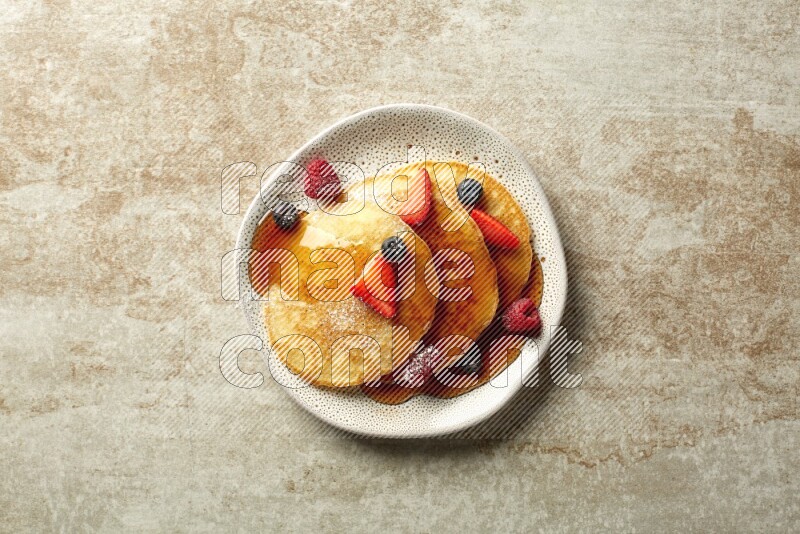 Three stacked mixed berries pancakes in an irregular plate on beige background