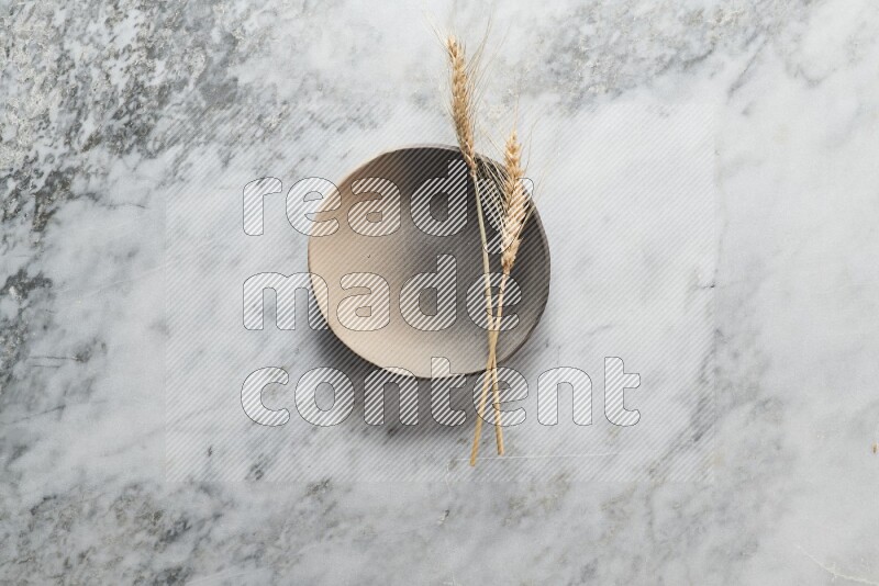 Wheat stalks on multicolored pottery plate on grey marble background
