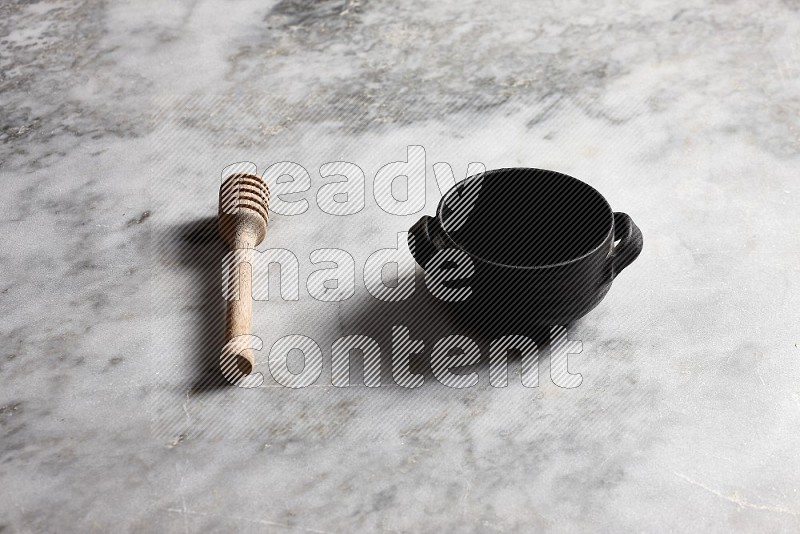 Black Pottery bowl with wooden honey handle on the side with grey marble flooring, 45 degree angle