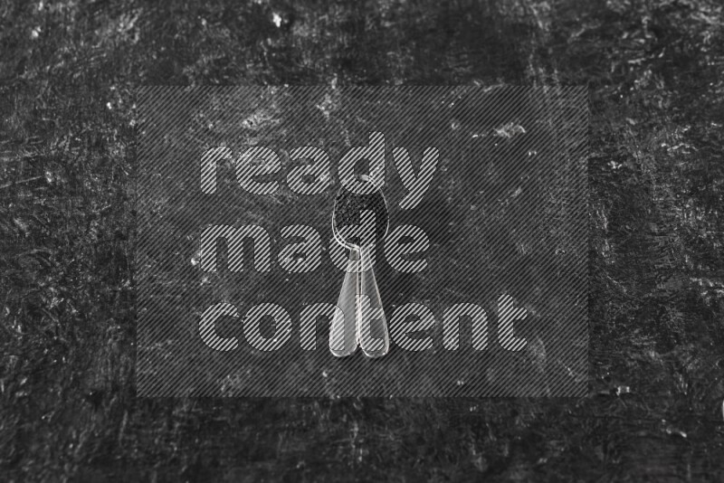 2 metal spoons full of black seeds on a textured black flooring