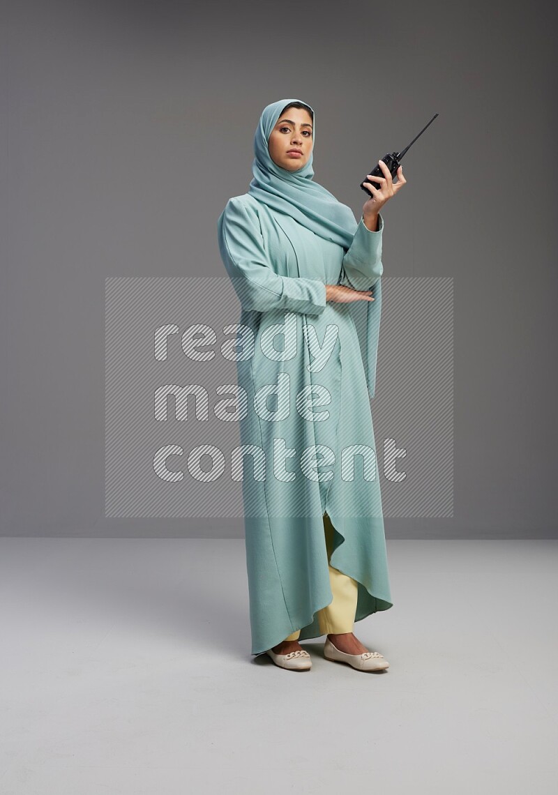 Saudi Woman wearing Abaya standing holding walkie-talkie on Gray background