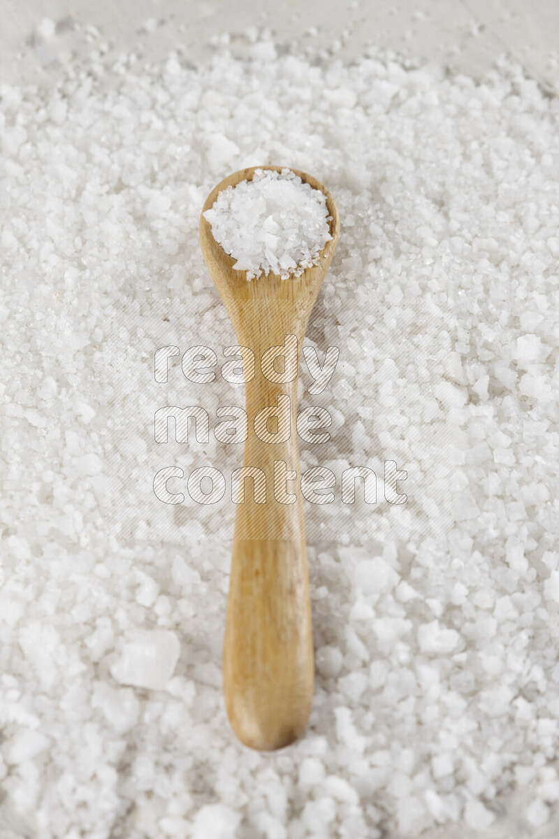 A wooden spoon full of white salt on white background