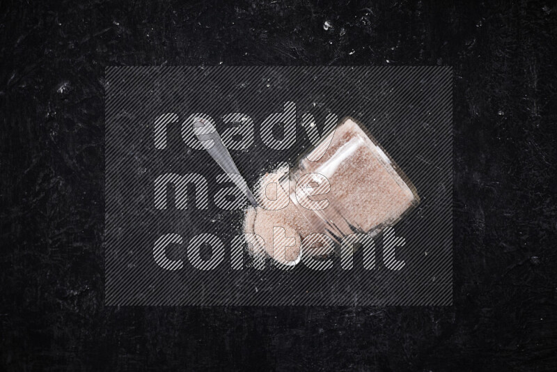 A glass jar full of fine himalayan salt on black background