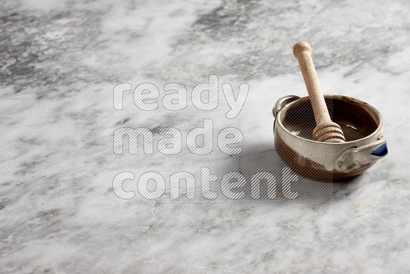 Multicolored Pottery bowl with wooden honey handle in it, on grey marble flooring, 45 degree angle