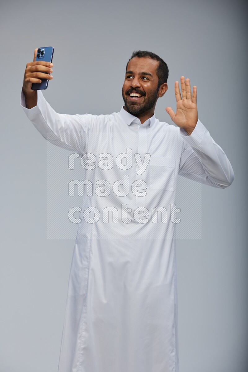 Saudi man wearing Thob standing taking selfie on Gray background