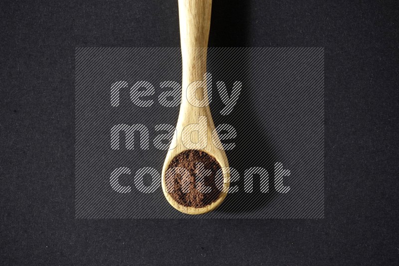 A wooden spoon full of cloves powder on a black flooring