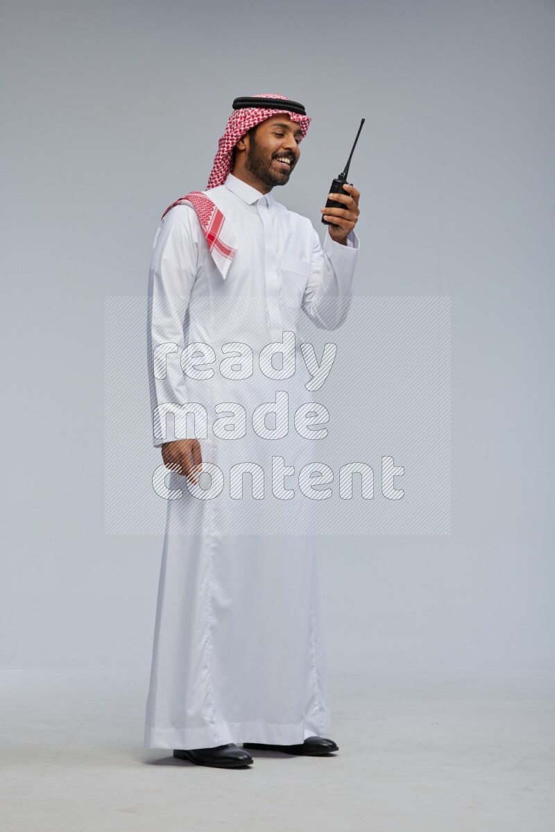 Saudi man Wearing Thob and shomag standing holding walkie-talkie on Gray background