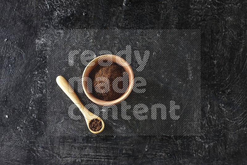 وعاء خشبي وملعقة خشبية ممتلئان ببودرة القرنفل على خلفية سوداء