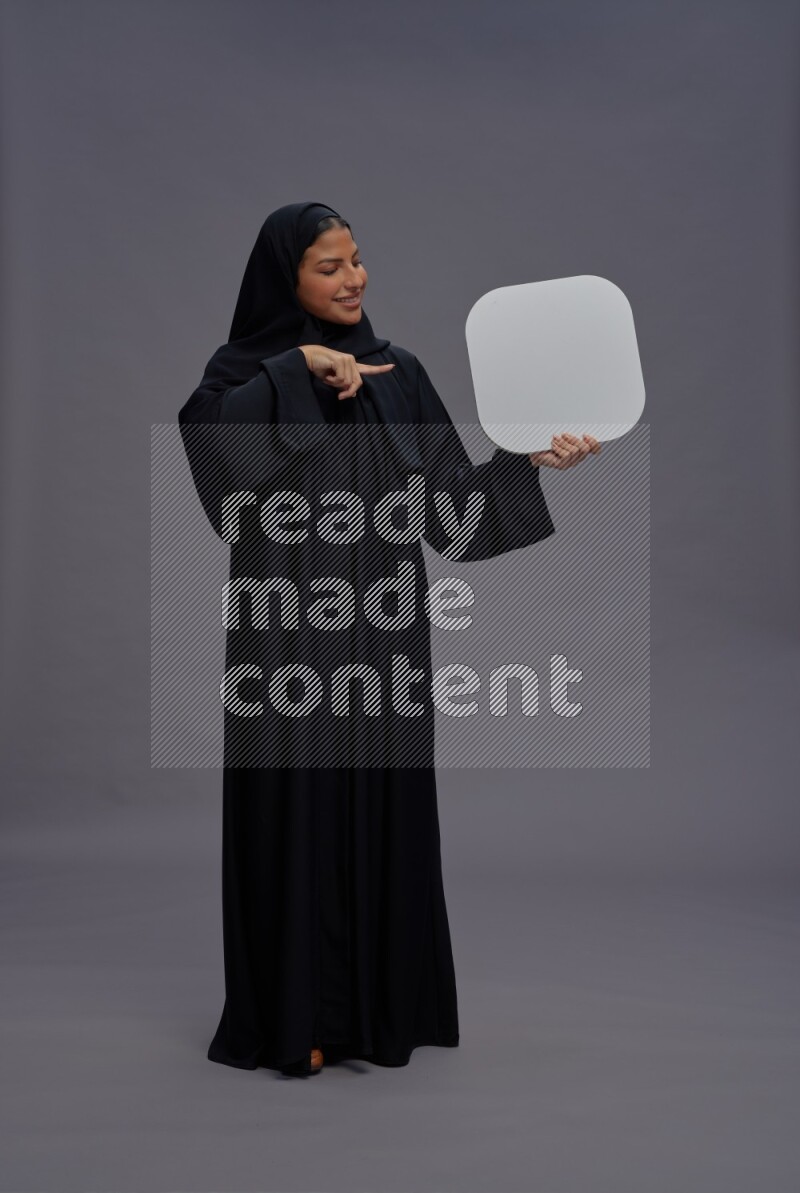 Saudi woman wearing Abaya standing holding social media sign on gray background