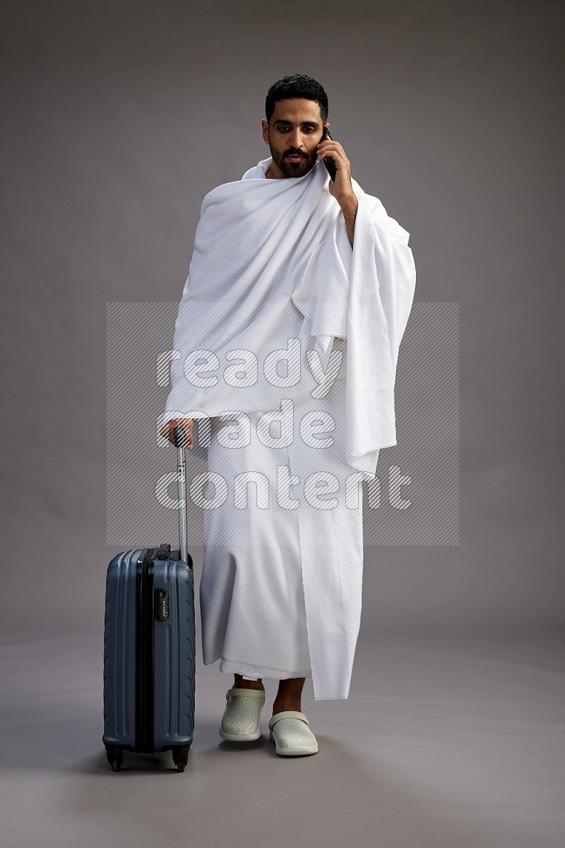 A man wearing Ehram Standing holding traveling bag on gray background