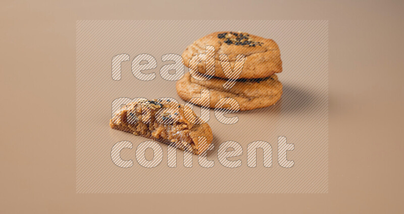 Two Hasawi cookies field of date and decorated by black seed and anise grain with another one cut in half on a brown background