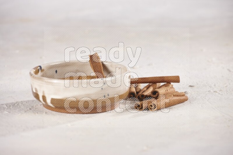 Ceramic bowl full of cinnamon powder with cinnamon sticks on the side on white background