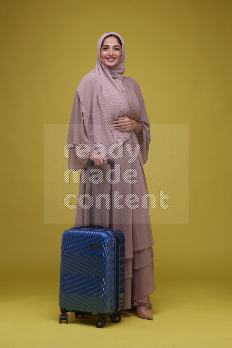 A woman With suit Case on a Yellow Background wearing Brown Abaya with Hijab