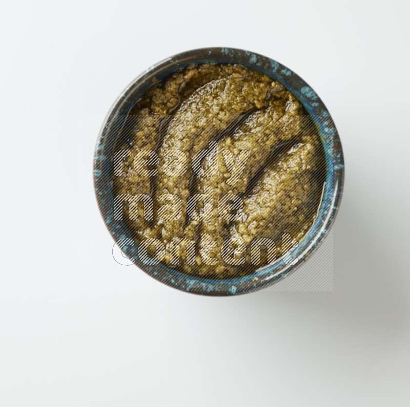Large multi color pottery round bowl filled with pesto paste on a white counter top