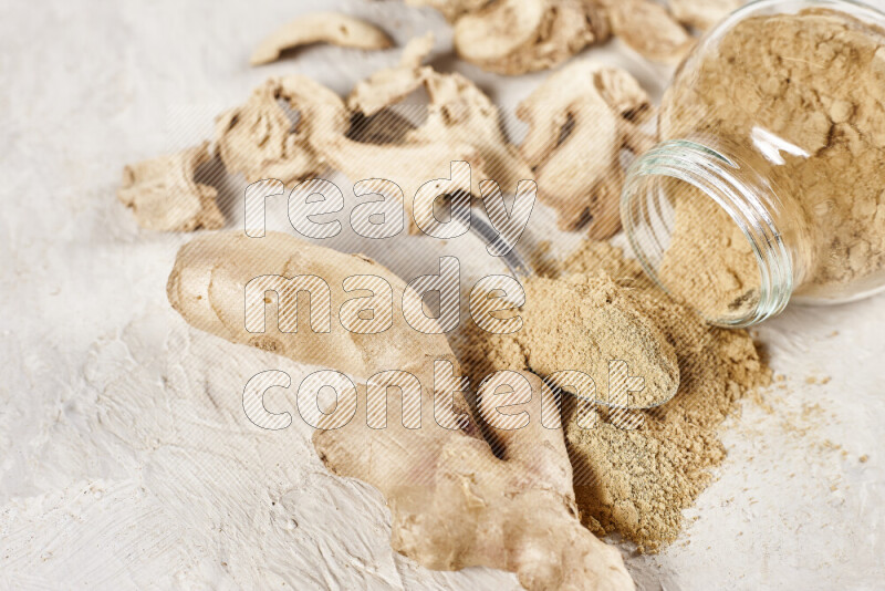 A glass jar full of ground ginger powder flipped with some spilling powder on white background