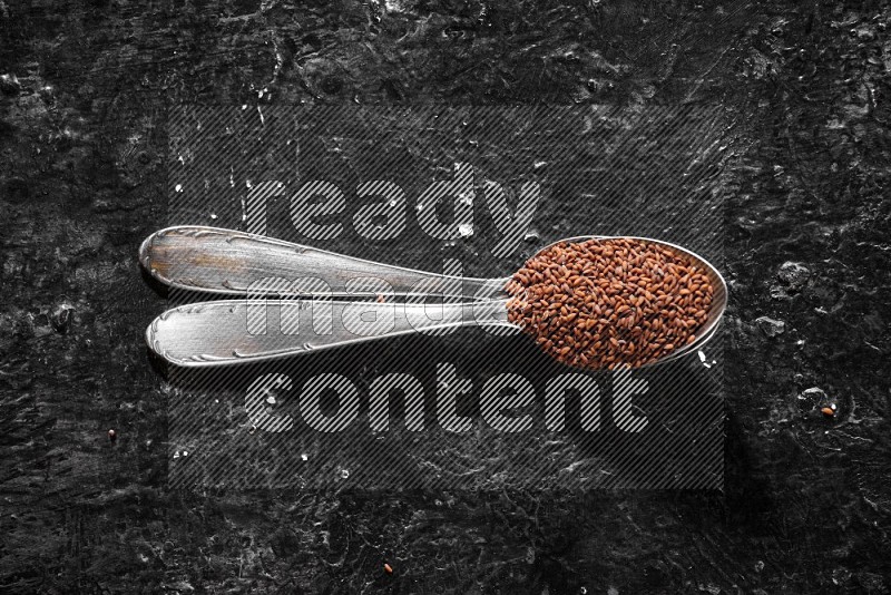 2 metal spoons full of garden cress seeds on a textured black flooring