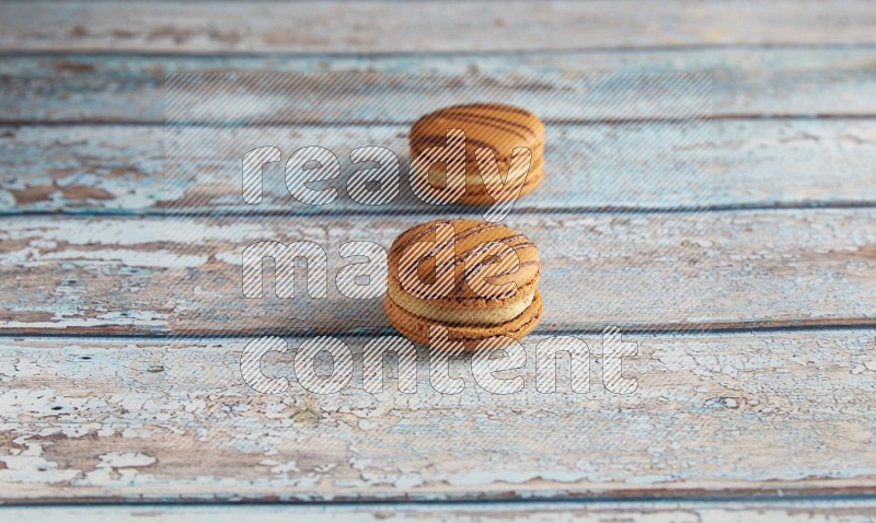 45º Shot of two light brown Almond Cream macarons on light blue wooden background