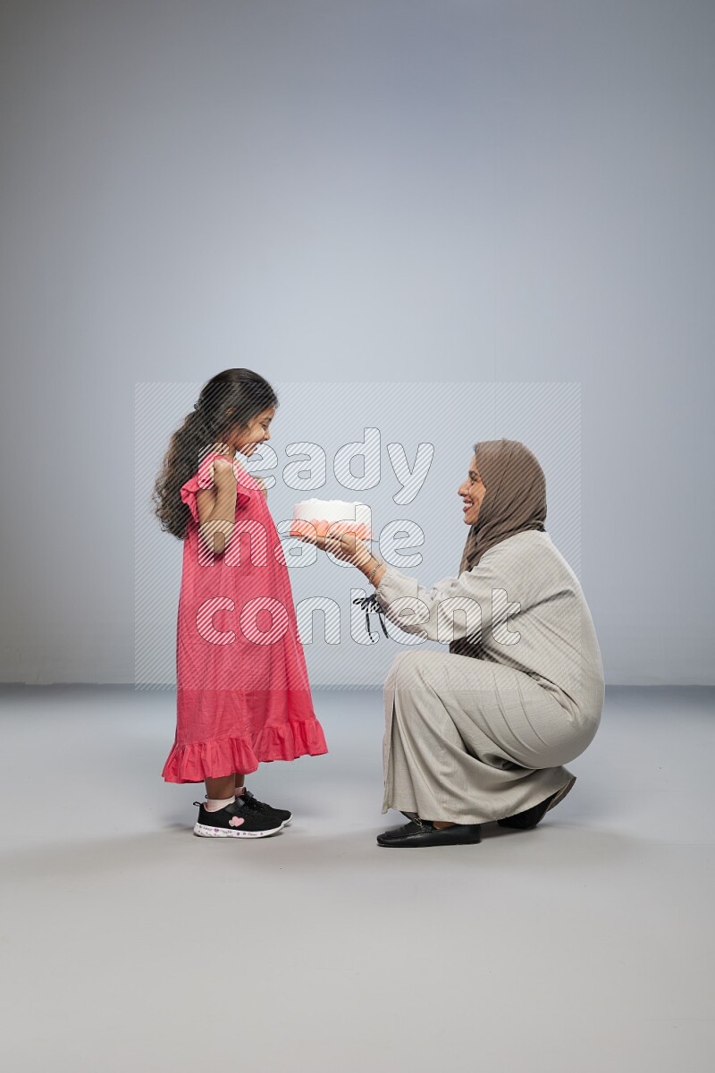 A mother giving a cake to her daughter on gray background