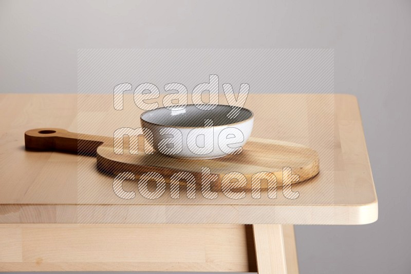 off white bowl placed on a  wooden oval cutting board on the edge of wooden table