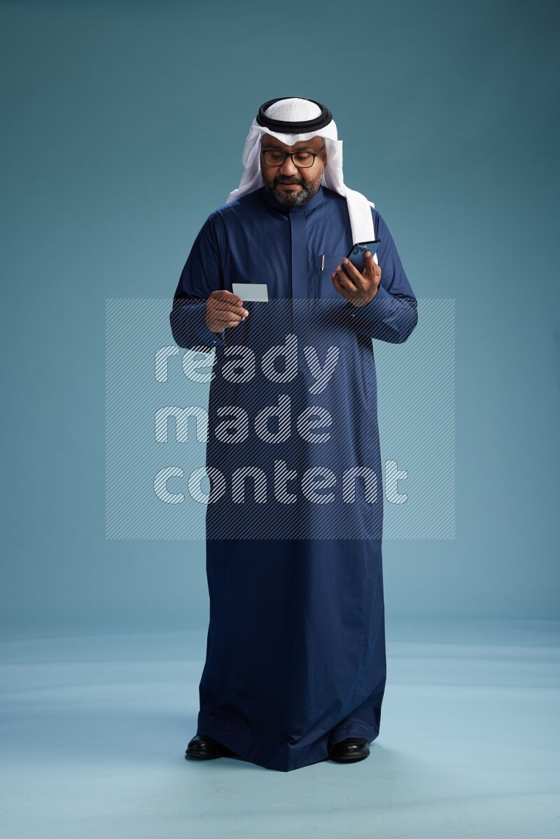 Saudi Man with shimag Standing holding ATM card while talking on phone on blue background