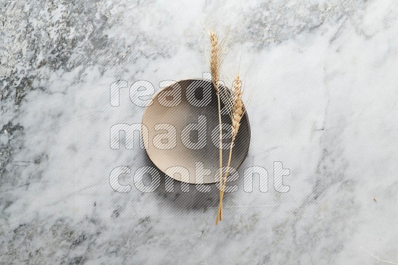 Wheat stalks on Multicolored Pottery Plate on grey marble flooring, Top view