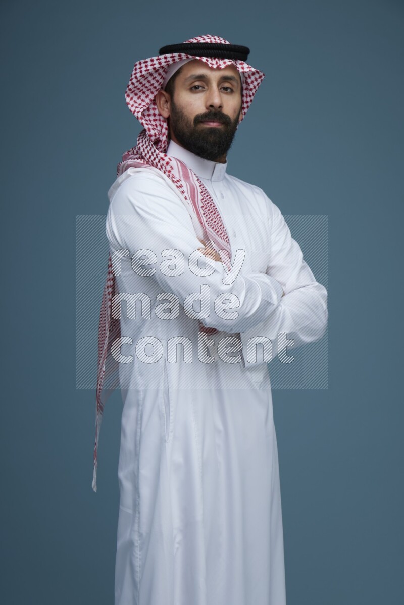 A man posing in a blue background wearing Saudi Thob and Shomag
