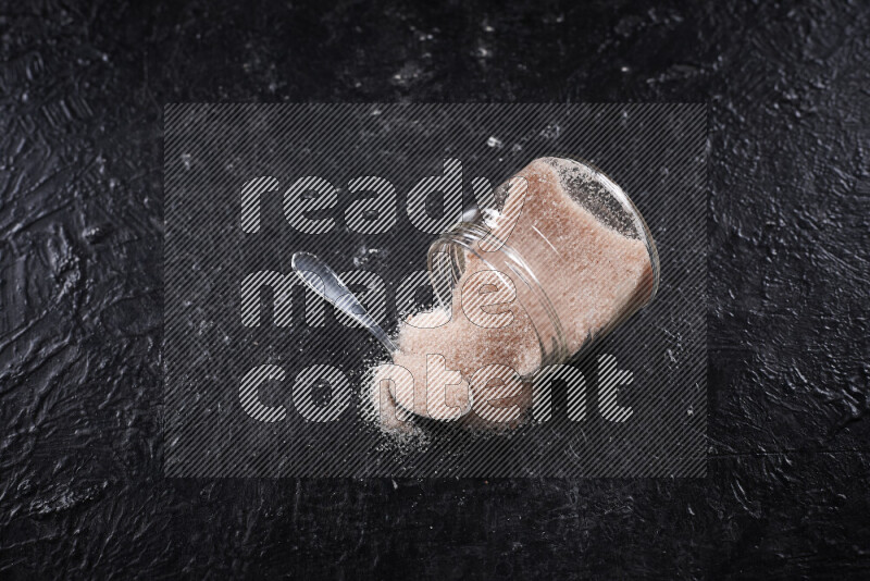 A glass jar full of fine himalayan salt on black background