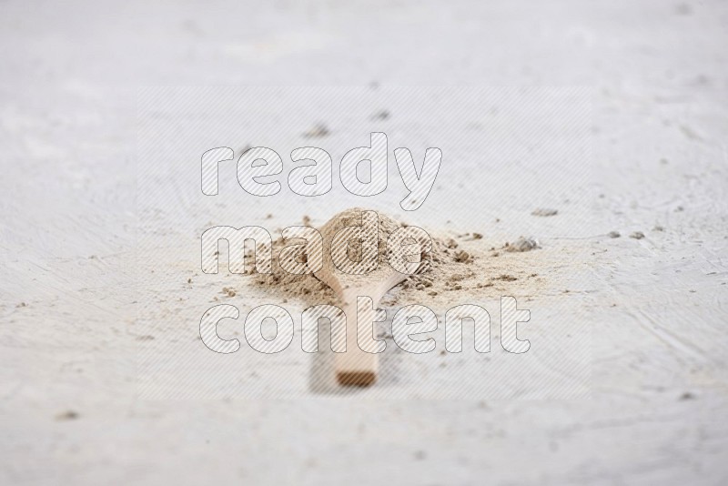 A wooden spoon full of garlic powder surrounded by the powder on a textured white flooring in different angles