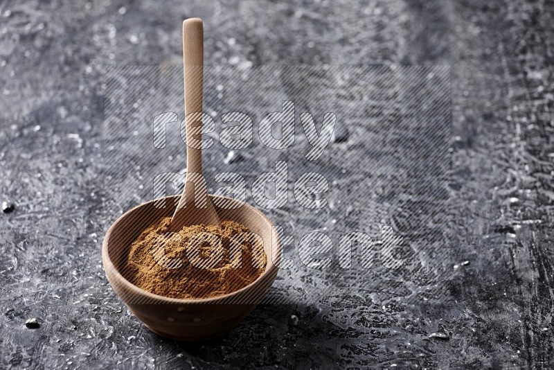 Wooden bowl full of cinnamon powder with a wooden spoon on a textured black background in different angles