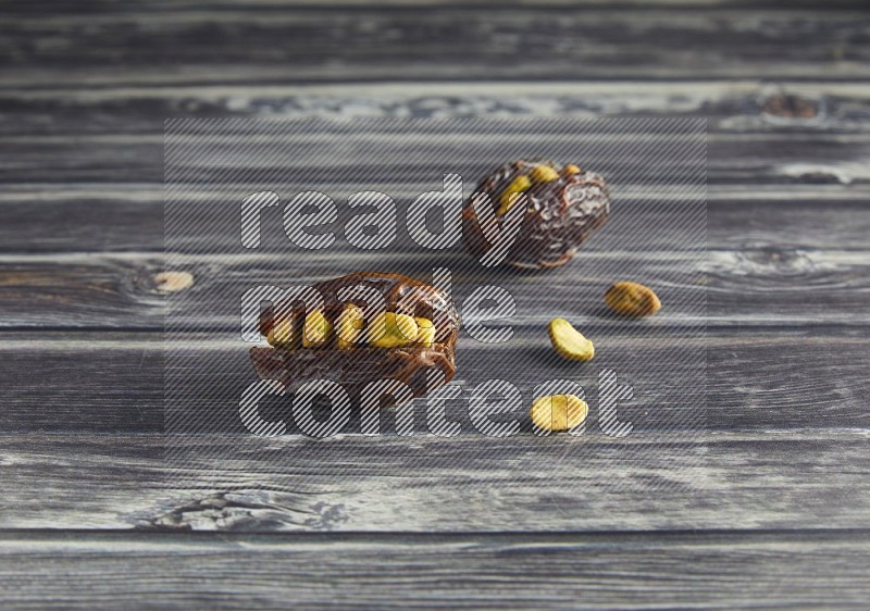 two pistachio stuffed madjoul dates on a wooden grey background