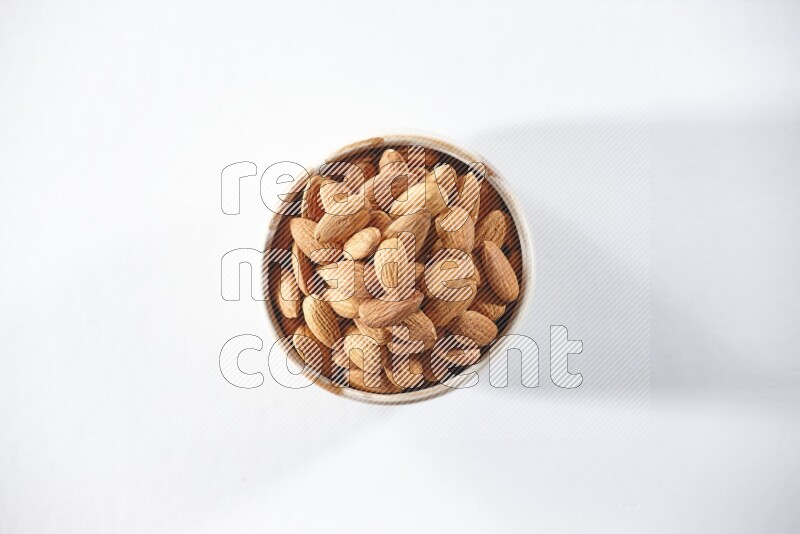 A beige ceramic bowl full of peeled almonds on a white background in different angles