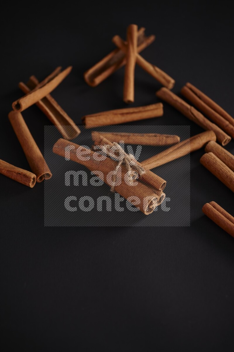 4 Cinnamon sticks stacked and bounded with more sticks in the background on black flooring