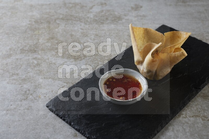 wonton cups with soy sauce ramkin on rectangle slate on grey textured counter top