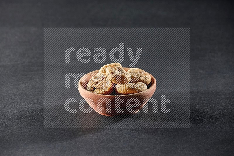 A wooden bowl full of dried figs on a black background in different angles