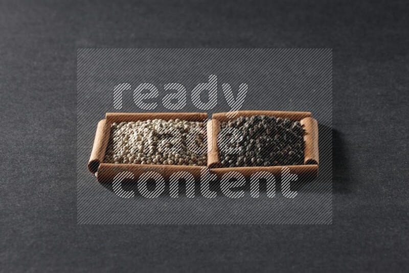 مربعان من أعواد القرفة ممتلئان بحبوب الفلفل الأبيض وحبوب الفلفل الأسود علي خلفية سوداء