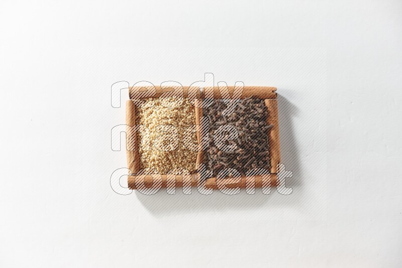مربعان من أعواد القرفة ممتلئان بالقرنفل وبذور السمسم علي خلفية بيضاء