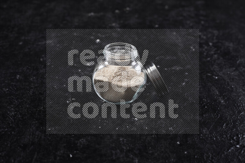 A glass jar full of onion powder on black background