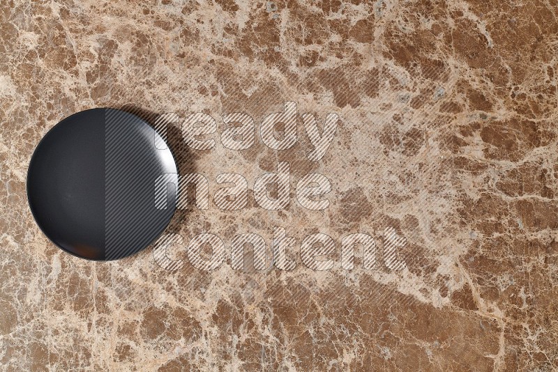 Top View Shot Of A Black Ceramic Circular Plate On beige Marble Flooring