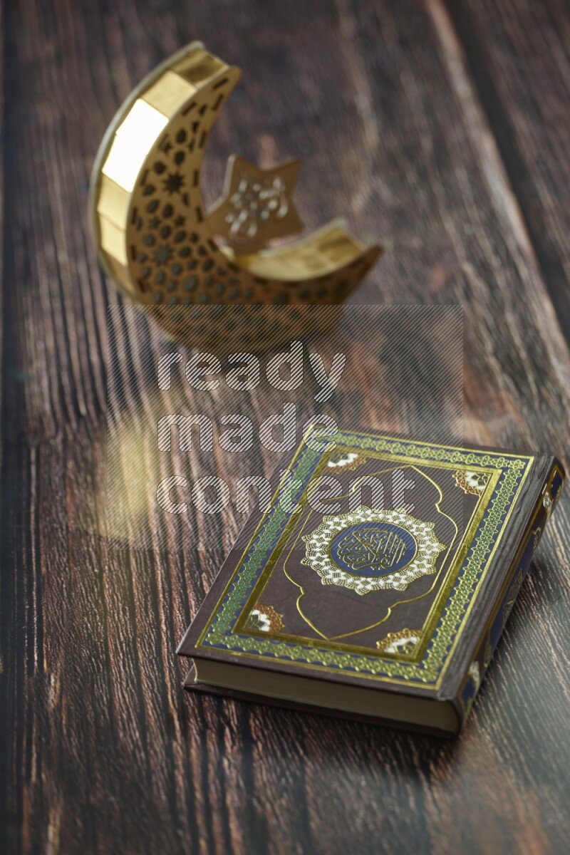 A wooden golden crescent lantern with different drinks, dates, nuts, prayer beads and quran on brown wooden background