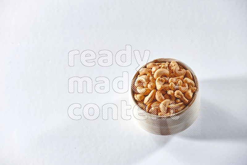 A beige ceramic bowl full of cashews on a white background in different angles