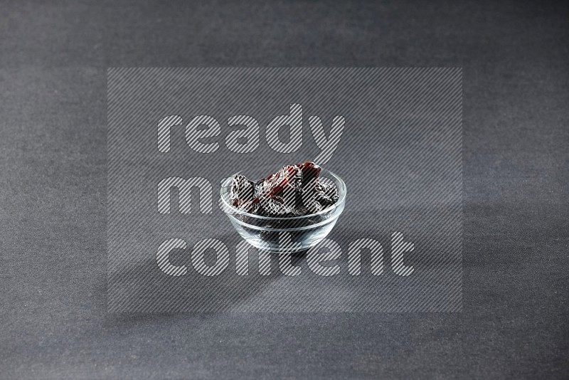 A glass bowl full of dried plums on a black background in different angles
