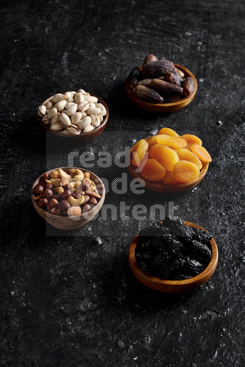 Dried fruits and nuts in wooden bowls in a dark setup