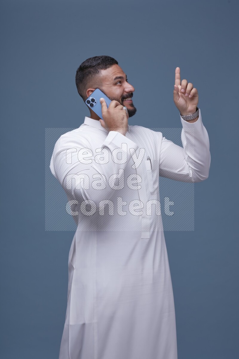 A Saudi man calling on blue background wearing Saudi Thob