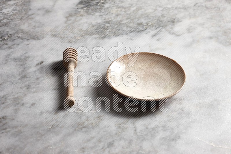 Beige Pottery Plate with wooden honey handle on the side with grey marble flooring, 45 degree angle