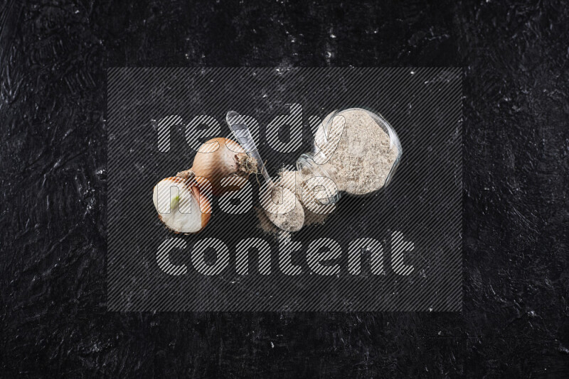 A glass jar full of onion powder flipped with some spilling powder on black background