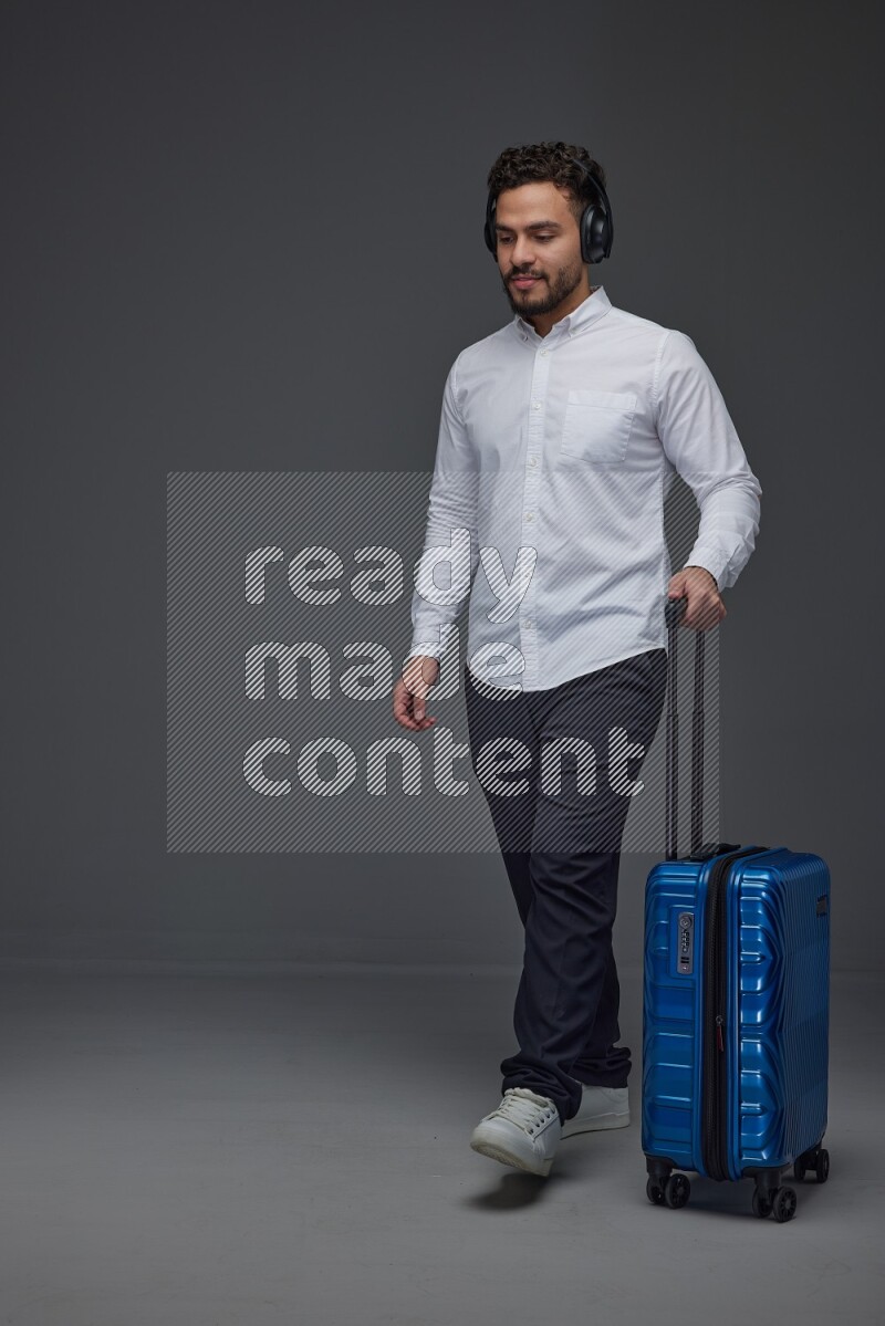 A man Posing with a carry-on with headsets  Wearing a White shirt on a grey background